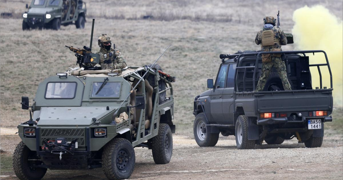 Soldados con uniforme de camuflaje participan en un entrenamiento militar al aire libre, utilizando vehículos todoterreno equipados con armamento y lanzando humo táctico amarillo.